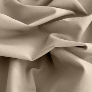 Peut inclure: Gros plan sur un tissu beige avec des plis et des ombres douces. Le matériau semble être un textile tissé, peut-être du lin ou du coton, avec une texture subtile. La couleur neutre et le drapé suggèrent qu'il pourrait être utilisé pour les vêtements ou la décoration intérieure.