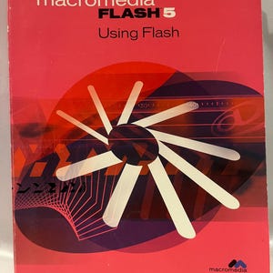 Könnte beinhalten: Buchcover für Macromedia Flash 5 mit dem Titel "Using Flash". Das Cover ist überwiegend rot mit einem großen weißen und lila Grafikdesign. Das Macromedia-Logo befindet sich unten rechts.
