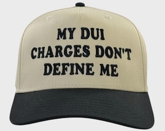 May include: A beige and black baseball cap with the text "MY DUI CHARGES DON'T DEFINE ME" embroidered in black. The cap has a curved brim and a button on top.