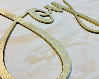 May include: Gold-colored wooden cutout of the word "Joy" on a light wood background.
