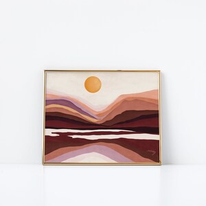 May include: Abstract landscape painting with a yellow sun and layered mountains in shades of brown, pink, and purple. The painting is framed in gold and has the artist's signature in the bottom right corner.