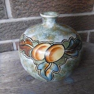 May include: A ceramic vase with a light blue glaze and brown, yellow, and blue painted floral designs. The vase has a round body and a narrow neck.