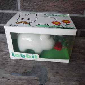 May include: A white Labbit soft vinyl toy in a clear plastic box with a green base. The box has the text "Labbit Make faces for happy mouths!" on the front.