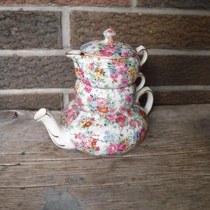 May include: Stacked floral teapot set with a teapot, a creamer, and a sugar bowl. The white porcelain set is decorated with a colorful floral pattern of pink, blue, yellow, and green flowers. The teapot has a gold trim.