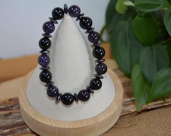May include: A black and purple beaded bracelet with alternating black and purple round beads. The bracelet is displayed on a small wooden stand.