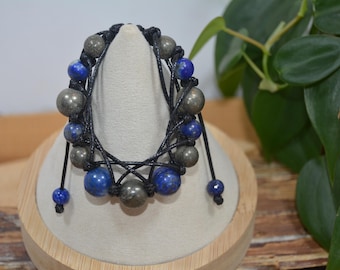 Pode incluir: Um bracelete de cordão preto com contas azuis e douradas. O bracelete é amarrado com um nó e tem uma borla em cada extremidade.