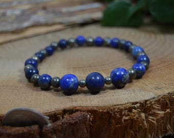 Pode incluir: Uma pulseira de contas com lápis-lazúli azul profundo e contas de pirite prateadas. A pulseira é exibida em uma superfície de madeira rústica, mostrando as texturas e cores naturais das pedras preciosas.
