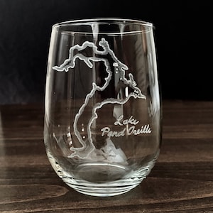 May include: A clear glass wine glass with an etched design of Lake Pend Oreille. The lake is outlined in white and the name of the lake is etched below the outline.