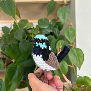 May include: A crocheted bluebird with a white belly, black wings, and a brown tail. The bird is being held in a person's hand.