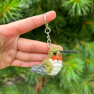 May include: A green, red, and white felt hummingbird keychain with a silver chain.