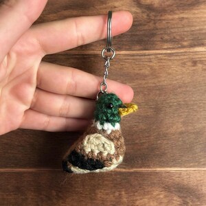 Puede incluir: Llavero de pato de ganchillo con cabeza verde, cuerpo marrón y beige y pico amarillo. El pequeño pato hecho a mano tiene un llavero de metal adjunto. Un accesorio encantador y caprichoso.