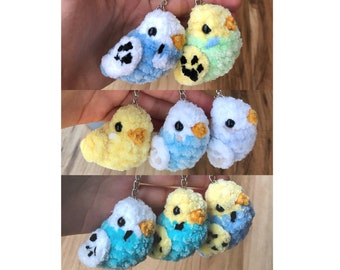Puede incluir: Un conjunto de seis llaveros de pájaros hechos a crochet. Los pájaros son de varios colores, incluyendo azul, amarillo y blanco. Cada pájaro tiene un pequeño ojo negro y un pico negro. Los llaveros están unidos a anillos plateados.