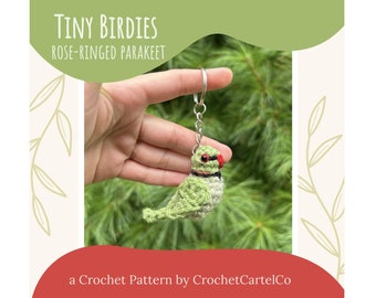 May include: Crochet pattern for a rose-ringed parakeet keychain. The parakeet is green with a red beak and black eyes. The keychain is made of yarn and is attached to a silver key ring.