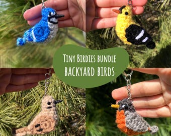 May include: A bundle of four crochet bird keychains. The birds are in various colors, including blue, yellow, brown, and gray, with black and orange accents. The text on the image reads "Tiny Birdies Bundle Backyard Birds" and "4 Crochet Patterns by CrochetCartelCo."