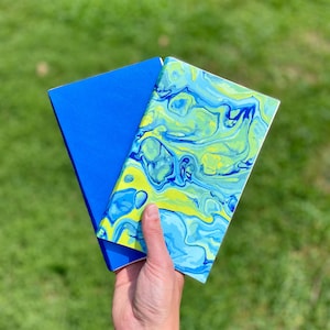 Peut inclure: Deux cahiers, l'un avec une couverture bleu unie et l'autre avec une couverture marbrée bleu et jaune.