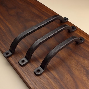 May include: Three black metal cabinet handles with a hammered, textured finish. Each handle features a curved arch design with two flat mounting ends, each containing a single circular screw hole for attachment to a surface.