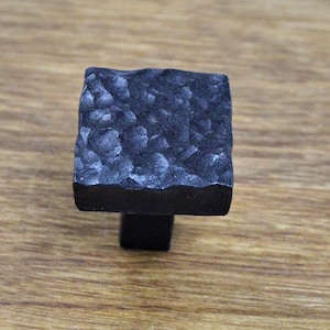 May include: A square black metal cabinet knob with a hammered finish.
