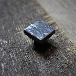 May include: A square, hammered metal cabinet knob with a textured surface.