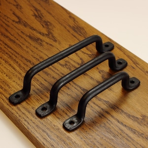 May include: Three matte black metal drawer pulls with a rounded, arched design. Each handle features two circular mounting points at the ends with pre-drilled holes for installation, showcasing a simple, functional, and sturdy construction.