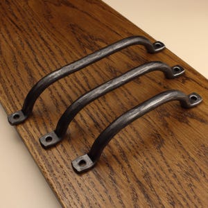 May include: Three dark grey metal cabinet handles with a hammered, textured finish. Each handle features a curved arch shape and two flat mounting ends, each containing a single circular screw hole for attachment to a surface or door.
