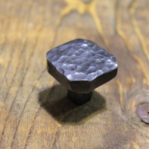 May include: A square-shaped, hammered metal cabinet knob with a textured surface. The knob is black and has a slightly rounded top.