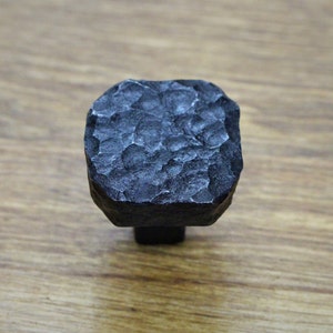 May include: A black square-shaped cabinet knob with a hammered metal finish.