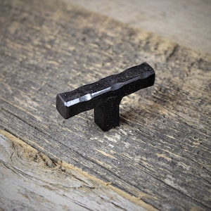 May include: Black metal T-shaped cabinet knob with a hammered finish.