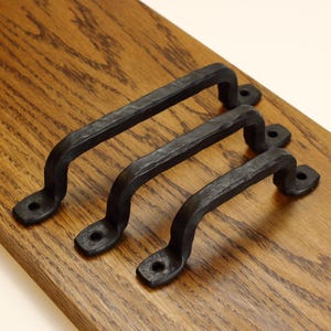 May include: Three black metal cabinet handles with a textured, hammered finish. Each handle features a curved arch design with two flat mounting ends, each containing a single circular screw hole for attachment to a surface or door.