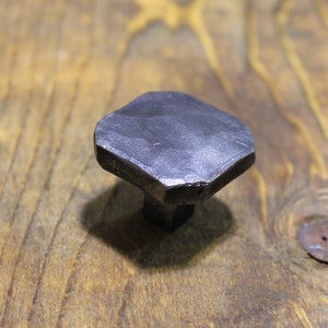 May include: A hexagonal metal knob with a smooth, dark grey finish. The knob is made of metal and has a slightly rounded shape.