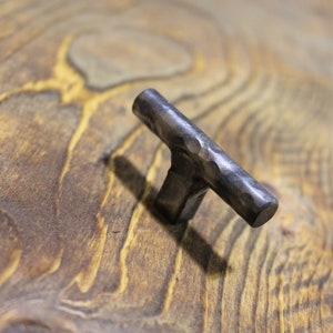 May include: A hammered metal cabinet knob with a textured finish. The knob is a dark grey colour and has a rectangular shape.