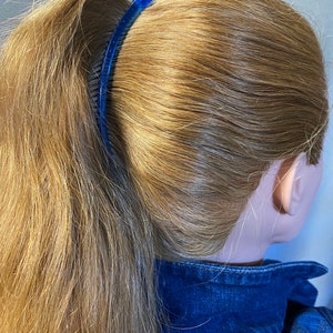Puede incluir: Un peine de pl&aacute;stico azul asegura una cola de caballo rubia. El peine es arqueado y tiene una serie de dientes. El cabello est&aacute; peinado en una cola de caballo alta, y el modelo lleva una chaqueta vaquera azul.