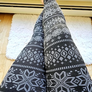 May include: Black leggings featuring a repeating gray geometric pattern of snowflakes, diamonds, and horizontal stripes. The fabric displays a consistent knit-like print across the entire surface, covering the legs from the ankles to the upper thighs.