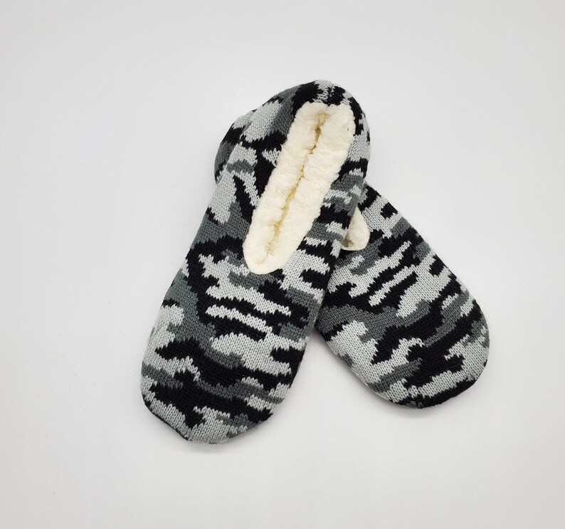 May include: A pair of black and gray camouflage slipper socks with a white fleece lining.