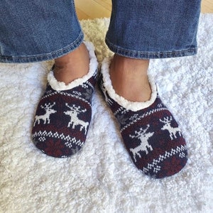 May include: A pair of cozy, fleece-lined slippers with a reindeer pattern in shades of blue, red, and white.