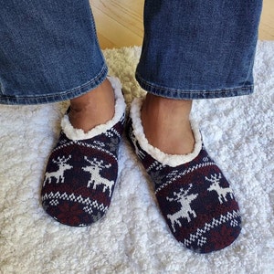 May include: A pair of blue and red slipper socks with a white reindeer pattern. The socks have a white fuzzy lining.