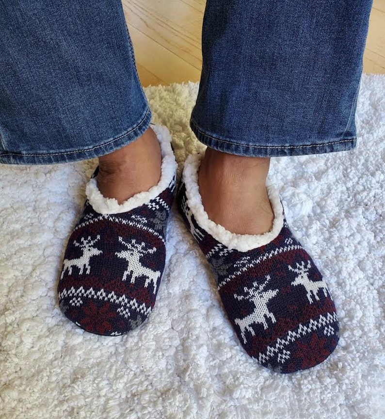 May include: A pair of blue and red slipper socks with a white reindeer pattern. The socks have a white fuzzy lining.