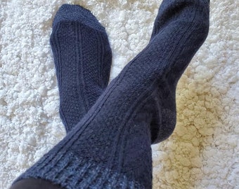 May include: A pair of dark blue knitted socks featuring a vertical ribbed texture and a cable knit pattern. The socks have a thick, elasticated cuff at the top and a reinforced heel and toe section, providing a textured appearance throughout the fabric.