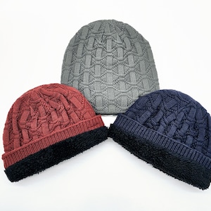 May include: Three knit beanies in gray, red, and navy blue. Each hat features a textured basketweave pattern on the crown, a ribbed knit band, and a thick black faux-fur lining along the interior edge, providing a layered look and texture.