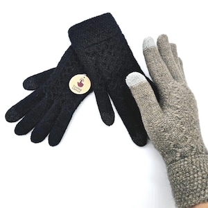 Może przedstawiać: Para czarnych rękawiczek z dzianiny z okrągłą metką z napisem Texting Gloves oraz pojedyncza rękawiczka z dzianiny w kolorze beżowego melanżu z jasnoszarymi końcówkami palców. Rękawiczki mają teksturowany wzór dzianiny do ekranów dotykowych.