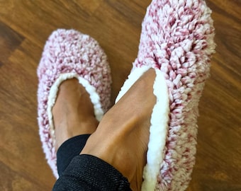 May include: A pair of plush, fuzzy slippers featuring a variegated pattern of dusty rose and white fibers. The interior lining is made of a soft, solid white material that creates a contrasting trim around the opening of each slipper.