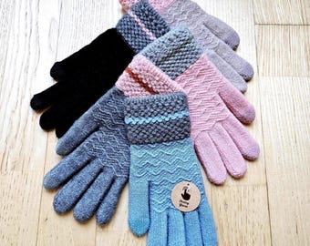 Può includere: Una collezione di guanti colorati lavorati a maglia in varie tonalità di blu, rosa, grigio e nero. I guanti presentano motivi strutturati e polsini a coste. Un paio ha una piccola etichetta rotonda con testo.