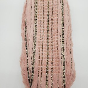 May include: A pink faux fur slipper with vertical gold and black leopard print stripes. The slipper has a textured sole with small, round, pink accents. The slipper is designed for comfort and style.