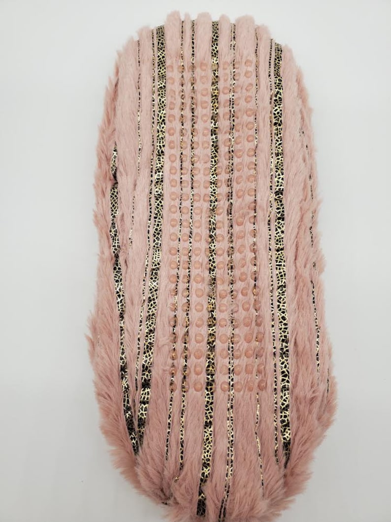 May include: A pink faux fur slipper with vertical gold and black leopard print stripes. The slipper has a textured sole with small, round, pink accents. The slipper is designed for comfort and style.