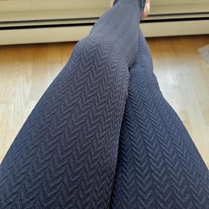 May include: A pair of dark navy blue leggings featuring a textured, raised chevron pattern that runs vertically along the length of the fabric. The leggings have a fitted silhouette and a consistent knit design throughout the entire garment surface.