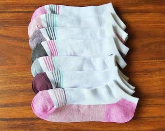 Puede incluir: Una pila de seis calcetines tobilleros, principalmente blancos con talones y punteras de colores. Cada par presenta un color de acento distinto, incluyendo rosa, gris claro, gris oscuro, azul claro, granate y rosa brillante, con rayas.