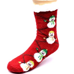 Puede incluir: Calcetines rojos y peludos de Navidad con un patrón de muñeco de nieve. Los calcetines tienen un puño blanco y peludo.
