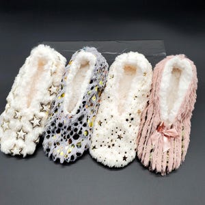 May include: Four pairs of cozy slipper socks in cream, gray, and pink. The cream-colored pair has gold star accents, the gray pair has gold dot accents, the other cream pair has gold star accents, and the pink pair has a bow.