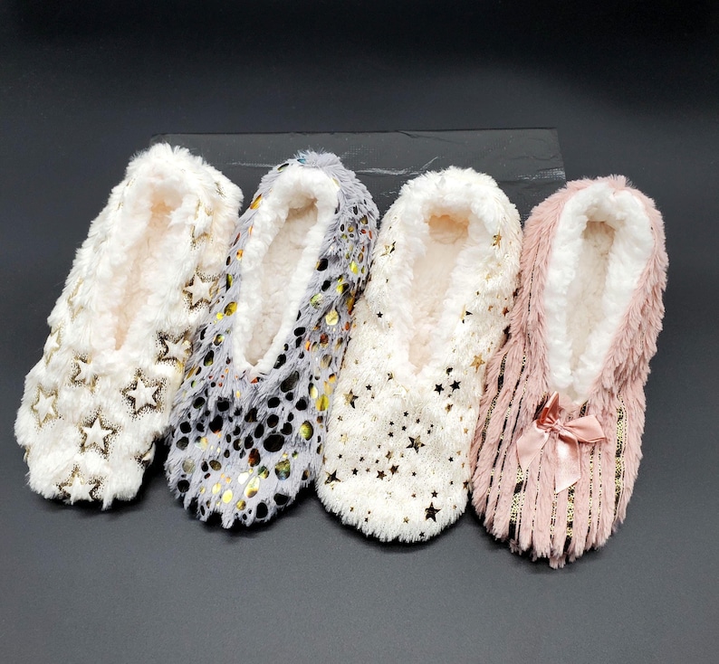 May include: Four pairs of cozy slipper socks in cream, gray, and pink. The cream-colored pair has gold star accents, the gray pair has gold dot accents, the other cream pair has gold star accents, and the pink pair has a bow.