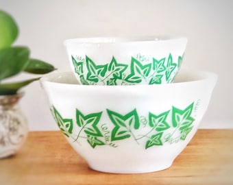 May include: Two white mixing bowls with a green ivy leaf design. The bowls are nested together.