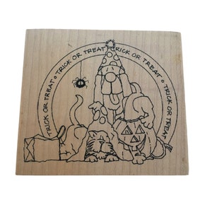 May include: A wooden rubber stamp with a black and white illustration of a cat, a dog, and a pumpkin wearing a party hat. The illustration is surrounded by a circle with the text "Trick or Treat" repeated four times.